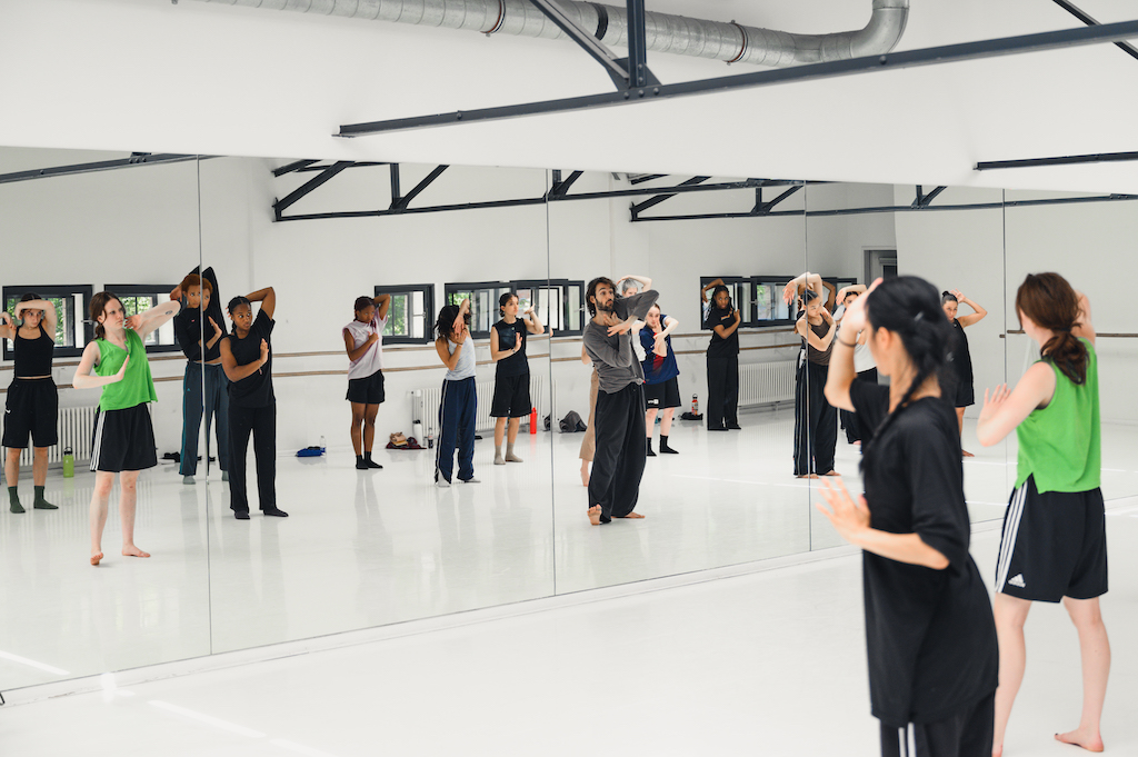 Dancers rehearse looking into a mirror in an open dance space
